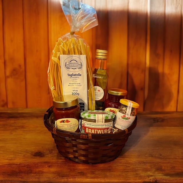 Geschenkkorb mit Flasche, Lebensmitteln und regionalen Produkten vor Holz­hintergrund.