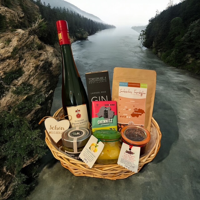 Geschenkkorb mit Weinflasche, Lebensmitteln und regionalen Spezialitäten in natürlicher Landschaft.